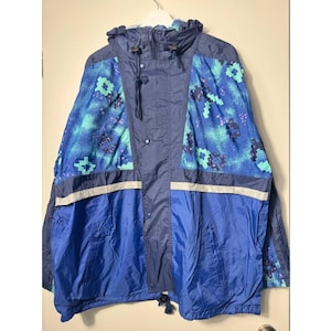 May include: A blue and navy hooded jacket with a reflective stripe. The jacket features a unique pattern of teal and purple floral shapes on the shoulders and upper back. The jacket is hanging on a white hanger.