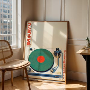 May include: A framed poster featuring a vintage turntable design. The artwork showcases a green vinyl record with a red center, a blue tone arm, and Japanese text. The poster is leaning against a wall next to a wooden chair.