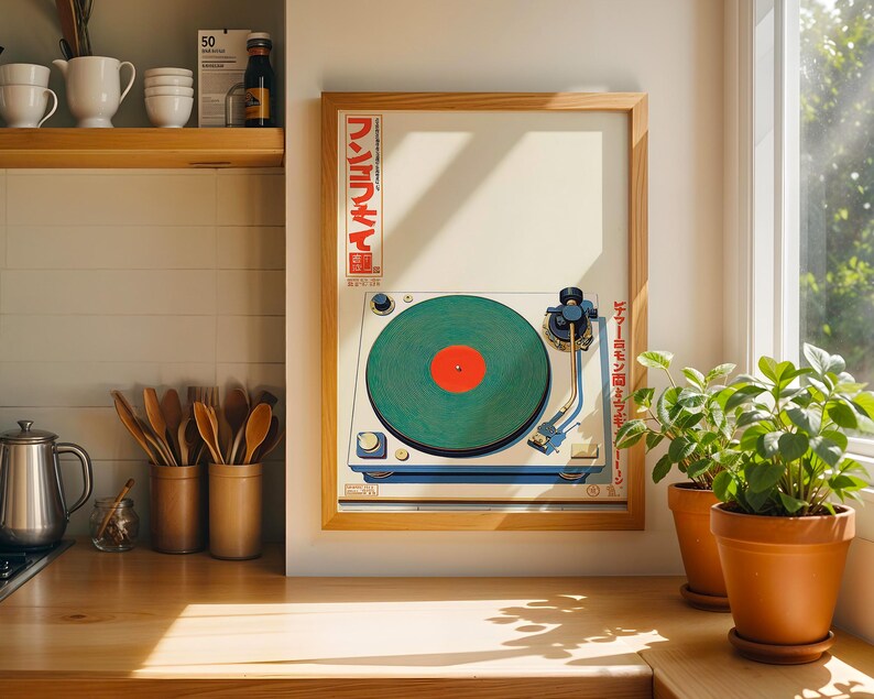 May include: A framed print of a vintage turntable with a green record and red center label. The print has Japanese text and is in a light wood frame. The image is displayed on a wooden countertop with potted plants nearby.