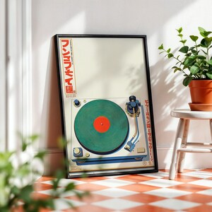 May include: Framed art print featuring a vintage-style turntable with a green record and red center. The artwork includes Japanese text in red and white. The print is displayed on a red and white checkered floor, next to a small white stool with a potted plant.