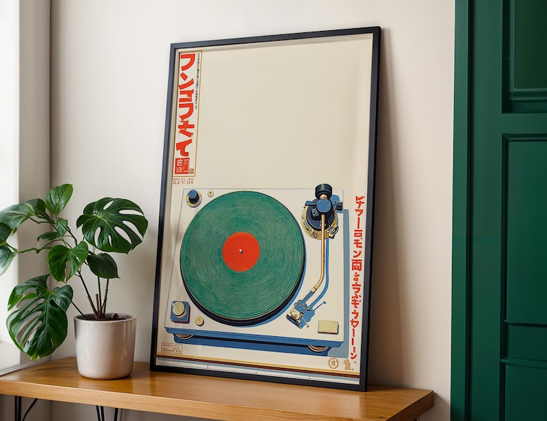 May include: A framed art print featuring a vintage-style turntable with a green record and red center. The turntable is set against a cream background with Japanese text on the side. The frame is black, and the artwork is displayed on a wooden surface.