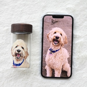 Puede incluir: Un tarro de cristal transparente con tapa de madera y un retrato pintado de un perro Goldendoodle con collar azul. Un smartphone muestra una imagen similar del perro. El perro tiene pelaje marr&oacute;n claro y est&aacute; sonriendo.