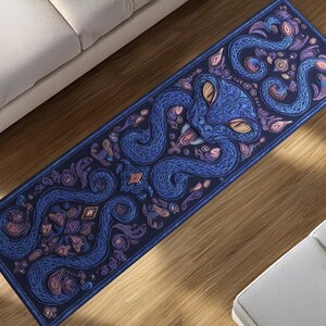 Könnte beinhalten: Eine rechteckige Yogamatte mit einer detaillierten Illustration eines blauen Oktopus mit orangefarbenen Augen und wirbelnden Tentakeln. Das Design umfasst lila und rosa florale Akzente auf einem dunkelblauen Hintergrund. Die Matte liegt auf einem Holzboden.