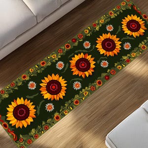 Puede incluir: Una alfombra rectangular con un fondo verde oscuro. La alfombra presenta grandes girasoles amarillos con centros marrones, rodeados por un borde de flores y hojas más pequeñas. La alfombra está colocada sobre un suelo de madera.
