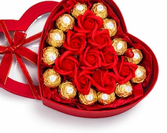 May include: A red heart-shaped gift box filled with gold-wrapped chocolates and red roses. The box is open, revealing the contents, and has a clear lid with a red ribbon tied on top. A romantic gift.