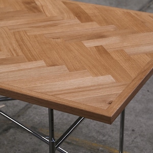 May include: A rectangular wooden table with a light brown, herringbone pattern tabletop. The table has a chrome-colored metal frame with four legs. The table is approximately 30 inches long and 20 inches wide.