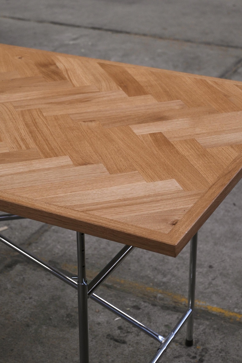 May include: A rectangular wooden table with a light brown, herringbone pattern tabletop. The table has a chrome-colored metal frame with four legs. The table is approximately 30 inches long and 20 inches wide.