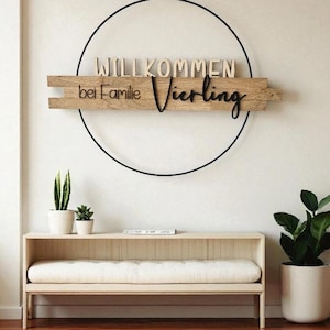 Könnte beinhalten: Ein Holzschild mit den Worten "WILLKOMMEN bei Familie Vierling" in einem kreisförmigen Design. Das Schild ist an einem dünnen Faden aufgehängt. Darunter befindet sich eine hellfarbene Holzbank mit weißem Kissen und Topfpflanzen.