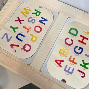 May include: Wooden alphabet puzzle with colourful letters. The puzzle features two wooden boards with the letters of the alphabet in various colours. The boards are set in a light-coloured wooden frame, designed for early learning and education.