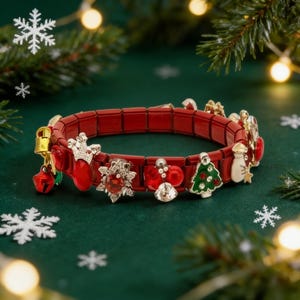 Puede incluir: Una pulsera roja con temática navideña con varios dijes, incluyendo una campana, un calcetín, un copo de nieve y un árbol de Navidad. La pulsera se muestra sobre un fondo verde con acentos de copos de nieve y ramas de pino.