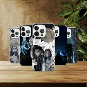 Puede incluir: Una colección de fundas para teléfonos con ilustraciones inspiradas en la película "La Novia Cadáver". Las fundas muestran personajes y escenas en escala de grises, con una luna llena y elementos góticos. Se exhiben sobre una superficie de madera.