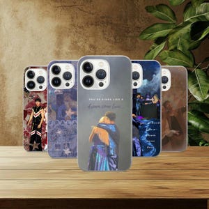 May include: Five phone cases with different designs are displayed. One case shows a person in a black and red outfit, another has a collage. The central case features an image of two people hugging with the text "You're kinda like a dream come true..."