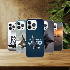 May include: A collection of phone cases featuring fighter jet designs. The cases display images of aircraft, with text including "F3", "J20", and "Chengdu J20". The cases are in various colors, including blue, gray, and white.