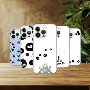 May include: Five phone cases with different designs are displayed. The cases showcase cartoon character illustrations and patterns, including black soot sprites, a blue case with colourful dots, and a white case with a Totoro design.