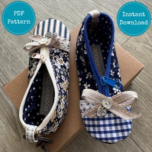 May include: Two fabric zip pouches with floral and striped patterns. One pouch features navy blue and white gingham with a blue zip, while the other has navy blue floral and striped fabric with a white zip. Both have beige bows and heart charms.