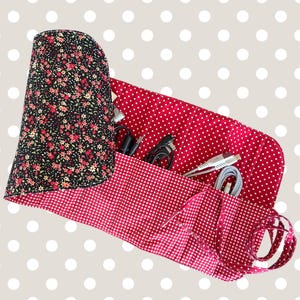 May include: A fabric roll-up organiser featuring a black exterior with a small floral print and a red interior with white polka dots and gingham patterns. The organiser contains multiple vertical slots holding various electronic charging cables.