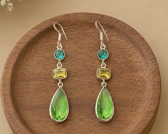 May include: A pair of silver drop earrings featuring a vertical arrangement of three faceted stones: a small round teal stone, a rectangular yellow stone, and a large pear-shaped lime green stone, all suspended from silver hooks.