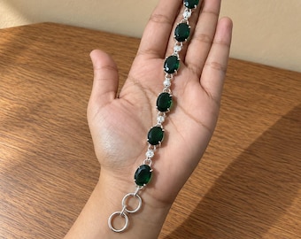 May include: A silver-toned bracelet featuring seven oval-shaped dark green stones arranged in a line. Each stone is separated by a small, clear, round accent stone. The bracelet includes a toggle clasp closure at one end with a circular ring.