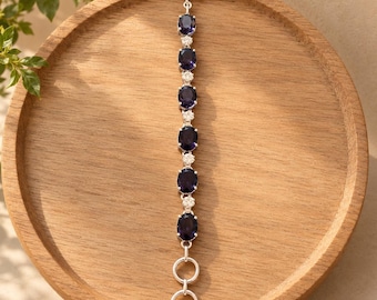 May include: A silver-toned bracelet featuring six oval-shaped deep purple stones alternating with small clear round stones. The piece includes a toggle clasp at the top and two circular links at the bottom for an adjustable fit.