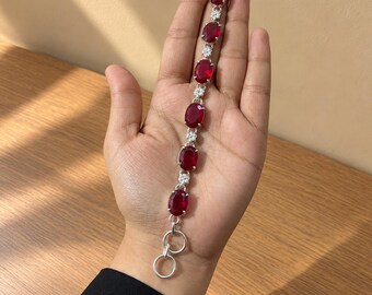 May include: A silver-toned bracelet featuring seven oval-shaped deep red gemstones arranged in a vertical line. Each red stone is separated by a small, clear, round accent stone. The bracelet includes a toggle clasp closure at the end.
