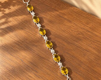 May include: A silver-toned bracelet featuring six oval-cut yellow gemstones set in metal frames, alternating with small silver flower-shaped links. The bracelet includes a circular ring clasp at one end and a T-bar toggle closure at the other.