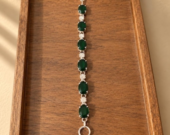May include: A silver-toned bracelet featuring six oval-shaped dark green stones arranged in a vertical line. The stones are separated by small, intricate silver-toned floral-shaped metal links. The bracelet includes a toggle clasp closure at the end.