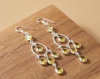 May include: A pair of silver chandelier earrings featuring multiple teardrop-shaped yellow gemstones. Each earring has a hook wire and a tiered design with several faceted stones suspended in a delicate metal frame, creating a dangling effect.