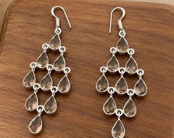 May include: A pair of silver chandelier earrings featuring multiple teardrop-shaped smoky quartz gemstones arranged in a tiered, cascading pattern. Each earring hangs from a simple silver hook and displays a polished metallic finish.
