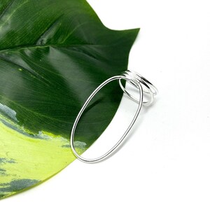 Könnte beinhalten: Ein Satz silberner Ringe mit ovalem Design. Die Ringe werden auf einem grünen Blatt mit weißem Hintergrund präsentiert. Die Ringe sind aus glänzendem Metall gefertigt.