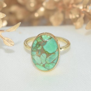 Op de afbeelding: Een gouden ring met een ovale, lichtgroene steen met bruine en gouden adering. De ring heeft een eenvoudige, gepolijste gouden band. De steen is het middelpunt, gezet in een gouden bezel.