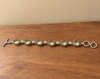 May include: A silver-toned bracelet featuring six oval-shaped, pale yellow gemstones alternating with small, clear, round stones. The piece is finished with a toggle clasp consisting of a T-bar and a circular ring at the opposite end.