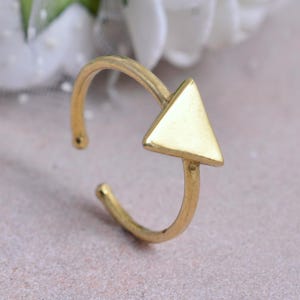 Könnte beinhalten: Ein goldfarbener, verstellbarer Ring mit einem dreieckigen Design. Der Ring hat ein gebogenes Band, das sich um den Finger legt, mit einem kleinen Dreieck an der Oberseite. Der Ring besteht aus einem glänzenden, metallischen Material.