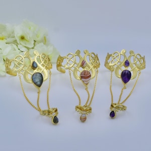 May include: Three gold-toned metal slave bracelets featuring intricate openwork knot designs. Each bracelet has a central teardrop gemstone, with delicate chains connecting to a matching ring component adorned with a smaller teardrop stone.