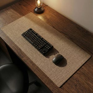 May include: A brown rectangular desk mat with a black keyboard and mouse on a wooden desk. The mat has a textured surface. A small lamp is visible in the background.