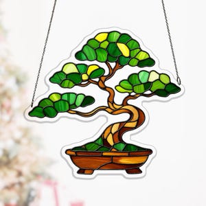 Może przedstawiać: Witraż przedstawiający drzewko bonsai z brązowym pniem i zielono-żółtą koroną. Drzewko znajduje się w brązowej doniczce i wisi na srebrnym łańcuszku. Szkło to mozaika kolorów i kształtów.