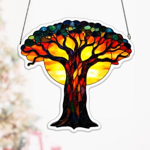 Op de afbeelding: Een glas-in-lood zonnevanger in de vorm van een boom met een levendige kroon van rode, oranje en gele glasstukjes. De stam is samengesteld uit donkere, veelkleurige glasscherven en een heldere gele cirkelvormige zon bevindt zich achter de takken.