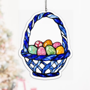 Könnte beinhalten: Ein dekorativer Osterschmuck in Form eines Korbes mit blauem geflochtenem Griff und Rand. Der Korb ist mit bunten, dekorierten Ostereiern in Rosa-, Orange-, Grün- und Gelbtönen gefüllt. Der Schmuck hängt an einer silbernen Kette.