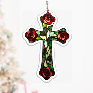 May include: A stained glass cross featuring red roses and green leaves. The cross is outlined in white and hangs from a silver chain. The roses are in full bloom, with detailed petals. The background is a soft white.