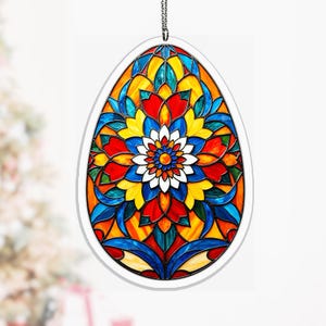 Könnte beinhalten: Ein eiförmiges Buntglas-Kunstwerk mit einem lebendigen Blumendesign. Das Kunstwerk hat einen weißen Rand und eine silberne Kette zum Aufhängen. Das Design enthält rote, gelbe, blaue und orange Farbtöne und schafft ein farbenfrohes und dekoratives Stück.