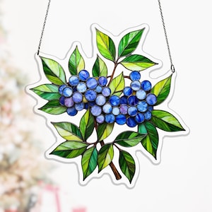 Pode incluir: Obra de arte em vitral com um cacho de bagas azuis e roxas com folhas verdes. As folhas têm detalhes em amarelo e verde. A obra é delineada em branco e pendurada por uma corrente. Uma peça decorativa.