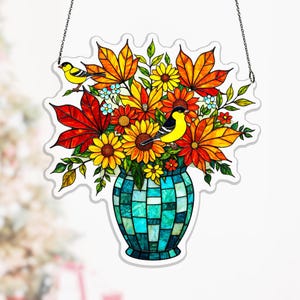 Pode incluir: Decoração de janela em vitral com um vaso cheio de flores coloridas e dois pássaros amarelos. O vaso é um mosaico de quadrados azuis e verdes. As flores são em tons de amarelo, laranja e vermelho, com folhas verdes.