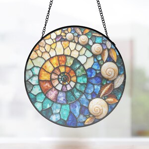 May include: A circular stained glass suncatcher featuring a central spiral ammonite pattern in shades of orange, yellow, blue, and purple. The design is accented with several small, light-colored spiral seashells and gold-toned leaf shapes, all suspended by a black metal chain.