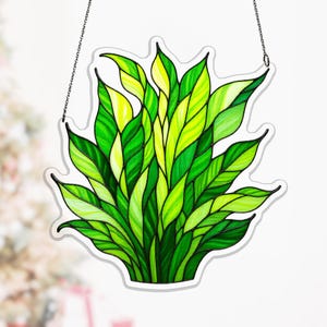 May include: A stained glass panel showing a cluster of green and yellow leaves. The leaves are various shades of green and yellow, with darker green veins. The panel is outlined in white and hangs from a chain.