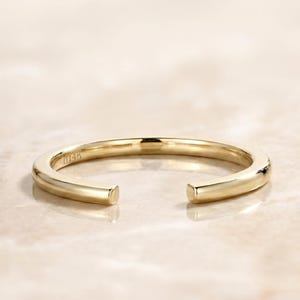 Op de afbeelding: Een goudkleurige open ring met een minimalistisch design. De ring heeft een glad, gepolijst oppervlak en een opening aan de voorkant. De ring staat tegen een neutrale achtergrond, wat de eenvoudige elegantie benadrukt. De ring is gemarkeerd met "14k".