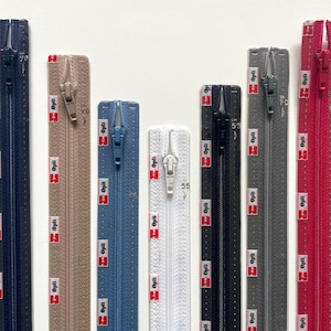 Puede incluir: Una variedad de cremalleras coloridas de diferentes longitudes. Las cremalleras son en tonos azul marino, beige, azul, blanco, negro, gris y rojo. Cada cremallera tiene un tirador de metal y está impresa con la palabra "Opti" y un logotipo rojo y blanco.