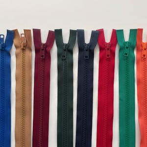 Può includere: Una collezione di cerniere colorate in varie tonalità, tra cui blu, beige, bordeaux, verde, blu navy, rosso, verde e arancione. Ogni cerniera è esposta verticalmente su uno sfondo bianco, mostrando il suo design aperto.