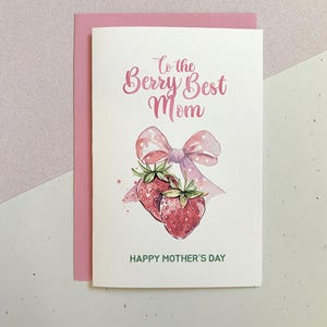 May include: A Mother's Day card with a pink envelope. The card features a watercolour illustration of two strawberries, a pink bow, and the text "To the Berry Best Mom" and "Happy Mother's Day" in pink and green.