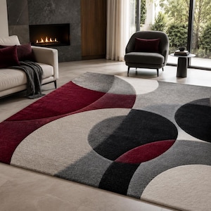Pode incluir: Um tapete retangular com um padrão geométrico de círculos e arcos sobrepostos em tons de bordô profundo, cinza-carvão, cinza-claro e creme. O design consiste em formas curvas arrojadas que criam um efeito visual de camadas sobrepostas.