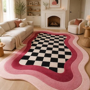 Könnte beinhalten: Ein Teppich mit wellenförmigen Rändern und einem Schachbrettmuster in Schwarz und Weiß in der Mitte, umgeben von rosa und roten Farbtönen. Der Teppich liegt auf einem hellen Holzboden und setzt einen Farbakzent in der neutralen Raumdekoration.