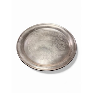 May include: A circular, silver-coloured metal tray with a raised edge. The tray has an embossed floral pattern in the centre. The tray is set against a white background.